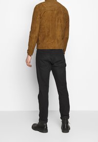 Södra bruna jacka med en slät textur, figursydd design och rak fåll, i kombination med svarta avsmalnande jeans och svarta ankelstövlar.