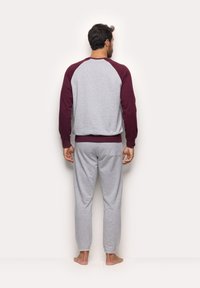 Sweatshirt gris avec des manches raglan bordeaux et une taille assortie, associé à un pantalon de jogging gris. Design décontracté avec des poignets élastiques.