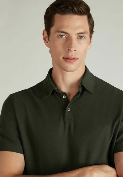 Polo de color verde oscuro hecho de tela suave con un cuello doblado y dos botones en el escote, con mangas cortas.