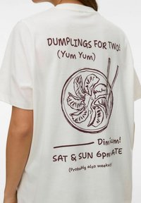 Biała bawełniana koszulka z brązowym nadrukiem graficznym przedstawiającym pierogi w misce z pałeczkami oraz tekstem o dim sum na plecach.