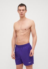 Shorts de sport violets avec une ceinture élastique, présentant un logo Nike blanc sur le côté gauche et une texture de tissu lisse et léger.
