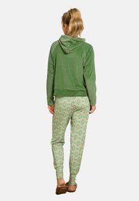 Grüne Velours-Cropped-Hoodie mit Kapuze, kombiniert mit grünen Jogginghosen mit floralen Mustern in Rot und Weiß, getragen mit hellen Schuhen.