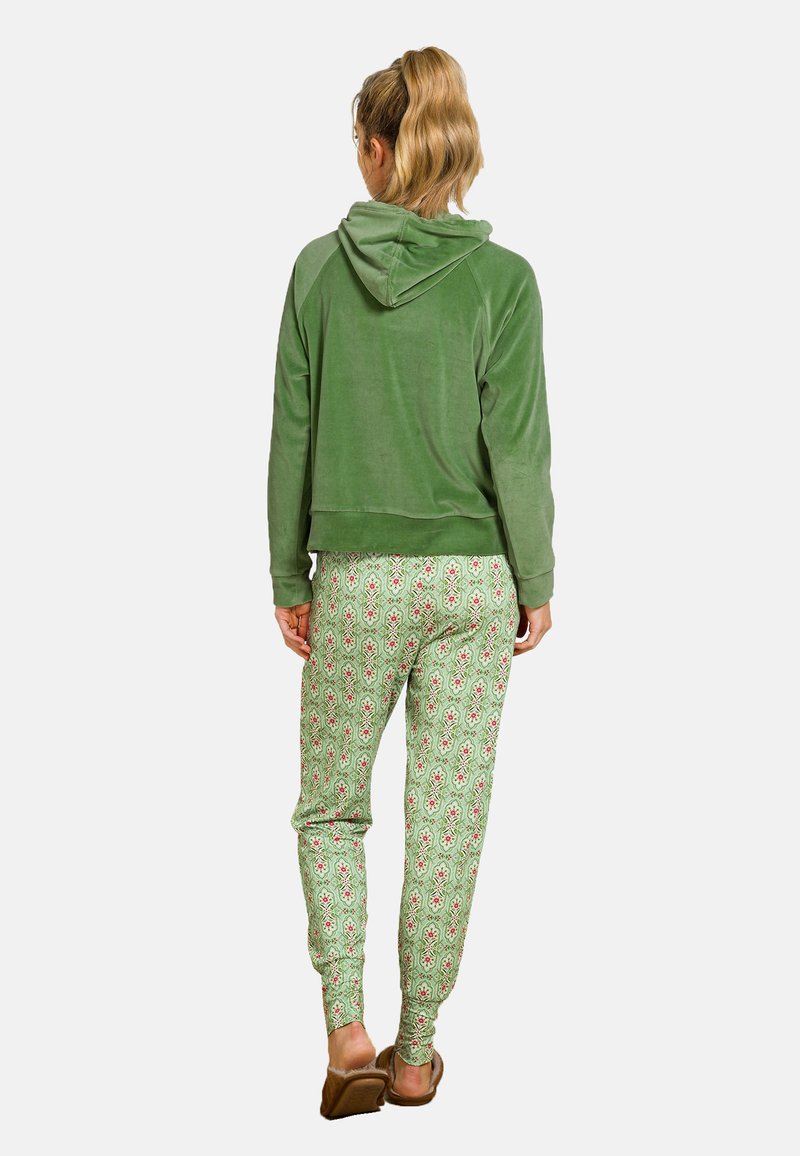 Grüne Velours-Cropped-Hoodie mit Kapuze, kombiniert mit grünen Jogginghosen mit floralen Mustern in Rot und Weiß, getragen mit hellen Schuhen.