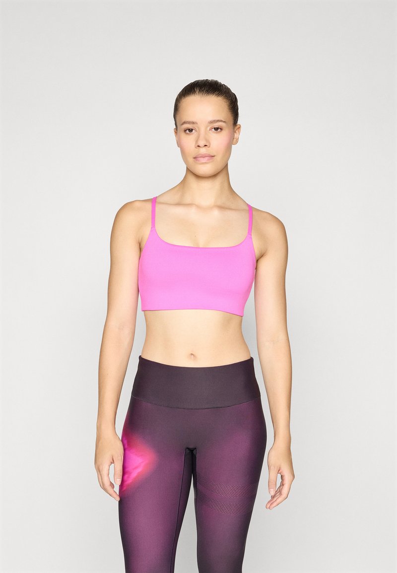 Rozā sporta krūšturis ar plānām siksniņām, apvienots ar augstiem tumšiem legingiem, kas izceļas ar gradientu un teksturētām akcentiem.