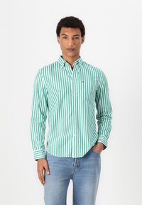 Cămașă button-up cu dungi verzi și albe, cu guler și un mic logo, asortată cu blugi decolorati. Material neted cu o croială clasică.