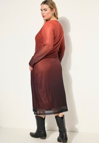 Mekko, jossa on pitkät hihat ja jonka väri vaihtelee tummasta punaisesta mustaan, valmistettu läpikuultavasta materiaalista, ja jossa on flare-helma, yhdistettynä mustiin cowboy-saappaisiin.