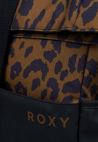Multicolore rugzak met een bruin en marineblauw luipaardprintpatroon met een textuur oppervlak; bevat een zwarte zak met het "ROXY" logo.