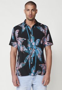 Camisa de manga corta con un fondo negro y patrones de palmeras en tonos rosa y azul. Confeccionada en un tejido ligero, con cierre frontal de botones.