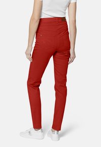 Pantalones ajustados rojos con una textura suave, bolsillos traseros con un sutil detalle de costura, combinados con zapatillas blancas.