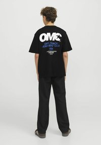 Juodas medvilnės marškinėliai su dideliu baltu "OMC" logotipu ir mėlynu tekstu ant nugaros, pasižymintys laisvu kirpimu ir trumpomis rankovėmis.