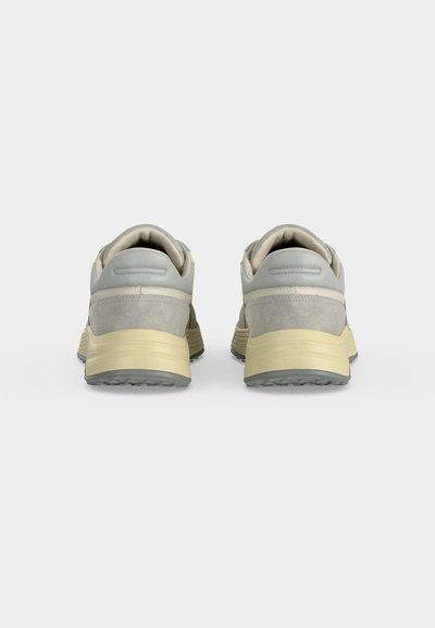 Paire de baskets grises et beiges vues de dos sur un fond uni gris clair.