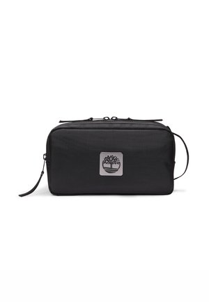 Sac noir, rectangulaire, en tissu durable, avec une plaque logo argentée et une fermeture à zip. Comprend une sangle de transport et une surface texturée.