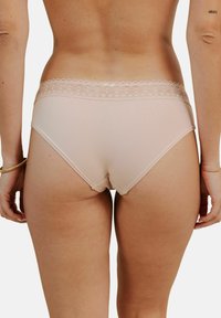 Culotte beige sans couture avec une bordure en dentelle le long de la taille, présentant une texture douce et une coupe taille moyenne pour plus de confort.