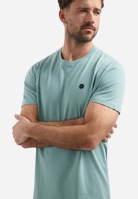 Lichtblauwe t-shirt met korte mouwen, gemaakt van zachte stof, met een klein zwart hexagonaal logo op de borst. Eenvoudig ronde hals ontwerp.