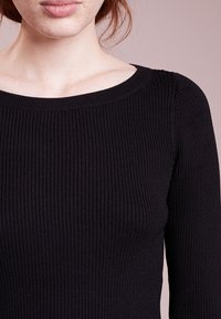 Svart ribbad långärmad topp med rund halsringning. Tyget verkar mjukt med en slät yta och ett jämnt ribbat mönster genom hela plagget.