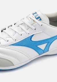 Vit sportig sko med blå mockadetaljer, gummisula och snördesign. Har sömnadsdetaljer och logotyp på tungan.