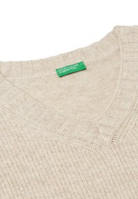 Světle béžový pletený svetr s výstřihem do V. Nabízí žebrovaný výstřih a lem. Na štítku je nápis "United Colors of Benetton" v zelené barvě. Měkounká textura.