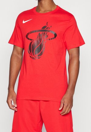 Homme portant un t-shirt rouge Nike avec un grand graphisme noir de basket-ball et de panier à l'avant, assorti à un short rouge assorti.
