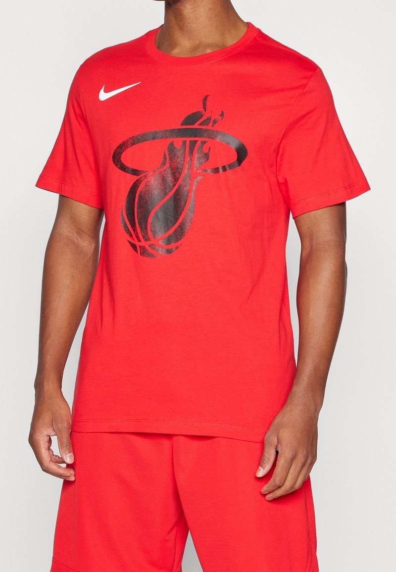 Homme portant un t-shirt rouge Nike avec un grand graphisme noir de basket-ball et de panier à l'avant, assorti à un short rouge assorti.