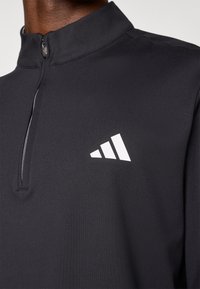 Black quarter-zip pullover made of smooth fabric, featuring a stand collar and a white Adidas logo with three stripes pattern on the chest.