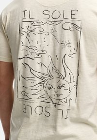 Bež majica s crnim crtežom sunca i oblaka, sa tekstom "IL SOLE" uklopljenim u grafički dizajn.