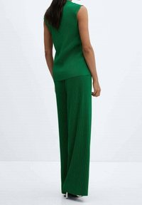 Haut sans manches côtelé vert associé à un pantalon large. Texture lisse, ajusté sur le haut, ample au niveau des jambes.