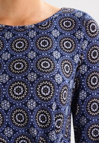 Blue fabric top with a circular black and white mandala pattern, scoop neckline, and soft texture. Geometric design with contrasting colors.
