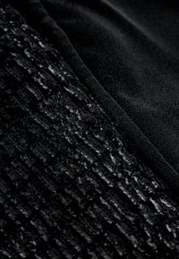 Must mustriga, millel on ühel küljel tekstuuritud muster ja teisel küljel sile viimistlus, tuues esile kontrastsed materjalid ja toonid.