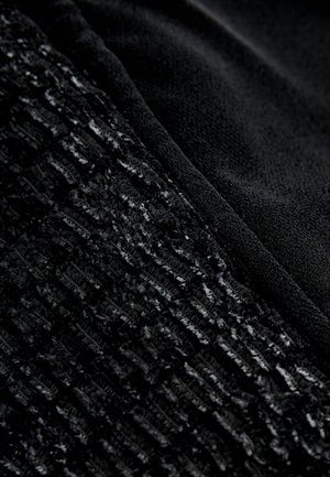 Čierna látka, ktorá na jednej strane zobrazuje textúrovaný vzor a na druhej hladký povrch, zdôrazňujúca kontrastné materiály a odtiene.
