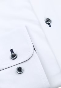 Witte shirt met een zak met klep, donkergijze knopen en subtiele zwarte stikdetails langs de rand. Gladde katoen stof.