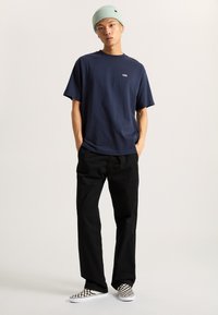 Navy cotton t-shirt with short sleeves and a small logo, paired with black trousers and black-and-white checkered slip-on shoes.