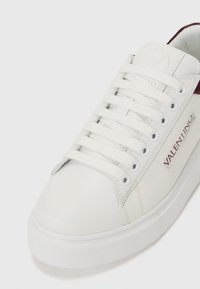 Witte leren sneaker met een ronde neus, witte veters en een kastanjebruine accent bij de hak. Beschikt over een merklabel aan de zijkant. Rubberen zool.