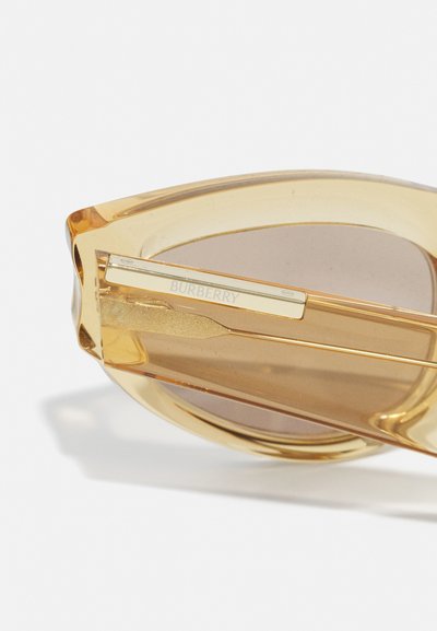 Burberry sunglasses with a transparent amber plastic frame, brown lenses, and a metallic gold-hued accent on the temple.