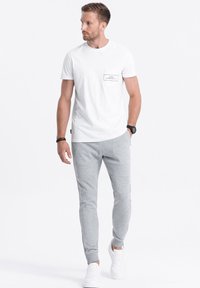White cotton t-shirt with a chest pocket and printed text, paired with light gray joggers featuring textured panels and white sneakers.