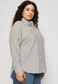 Striped button-up shirt in gray and white, featuring a structured collar and long sleeves, with a relaxed fit and side slits at the hem.