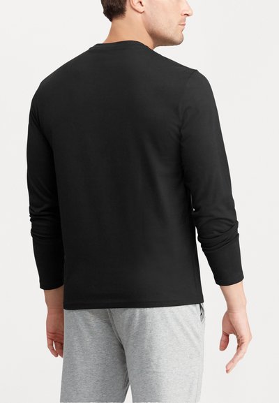 Camisa preta de mangas longas com decote redondo, textura suave e mangas ajustadas; combinada com calças cinza claro.