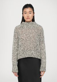 Chunky striktrøje i sort og hvid med høj hals, lange ærmer og ribbede manchetter. Tekstureret design med cropped pasform.