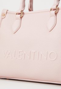 Rózsaszín bőrtáska texturált felülettel, arany árnyalatú szerelvényekkel és oldalán dombornyomott "VALENTINO" logóval.