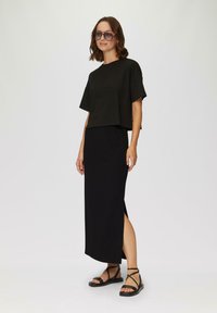 T-shirt noir cropped à manches courtes, associé à une longue jupe maxi noire avec des fentes sur les côtés. Porté avec des sandales noires à lanières.
