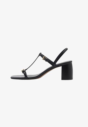 Svart klacksandals med T-remdesign, texturerade remmar och klack i blockstil. Utrustad med hardware i guldton och en slät sula.
