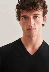 Schwarzer V-Ausschnitt-Pullover aus weichem Stoff, mit glatter Textur und taillierter Silhouette, die den Kragen und die Ausschnittdetails betont.