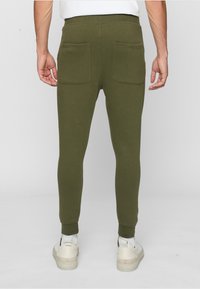 Olivgrüne tapered Jogginghosen aus Baumwolle, mit zwei Gesäßtaschen und elastischen Bündchen am Knöchel. Glatte Textur, taillierter Schnitt.