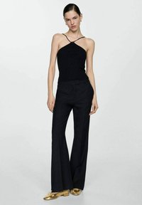 Črn rebrast top s halter vratom in tankimi naramnicami, v kombinaciji z visokim pasom črnimi širokimi hlačami in sijočimi zlatimi čevlji. Preprosta in elegantna zasnova.