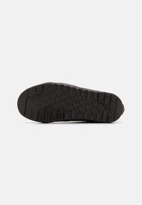 Semelle de chaussure noire avec motifs hexagonaux et linéaires, conçue pour l'adhérence et la durabilité, affichée sur fond blanc.