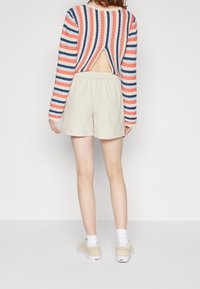 Pull en maille à rayures avec dos ouvert, associé à un short beige. Le pull présente des rayures rouges, bleues et crème, et des manches longues.