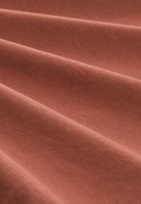 Weiche, glatte Stofffalten in einem warmen, gedämpften Terrakotta-Farbton, die subtile Texturen und sanfte Schatten zeigen.