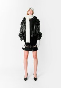 Chaqueta bomber de cuero negra con corte oversize, cuello alto y múltiples bolsillos. Falda corta negra con acentos de herrajes y gorro y guantes de punto blancos.