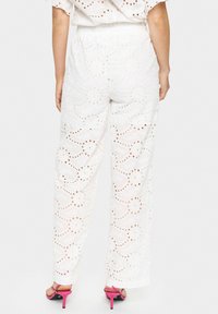 Witte broderie anglaise broek met een losse fit, voorzien van bloemmotieven en uitsnijdingdetails. Gecombineerd met roze hoge hakken sandalen.