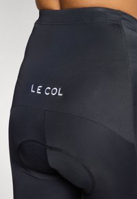 High-performance black cycling shorts with a smooth texture, featuring a logo "LE COL" in white embroidery and a chamois area for comfort.