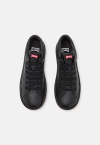 Černé kožené tenisky s texturovaným povrchem, s pevným šněrováním a červeným logem "Camper" na jazyku. Gumová podrážka s minimálním vzorkem.